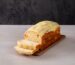 a loaf cake with yellow icing and sliced pieces on a wooden board