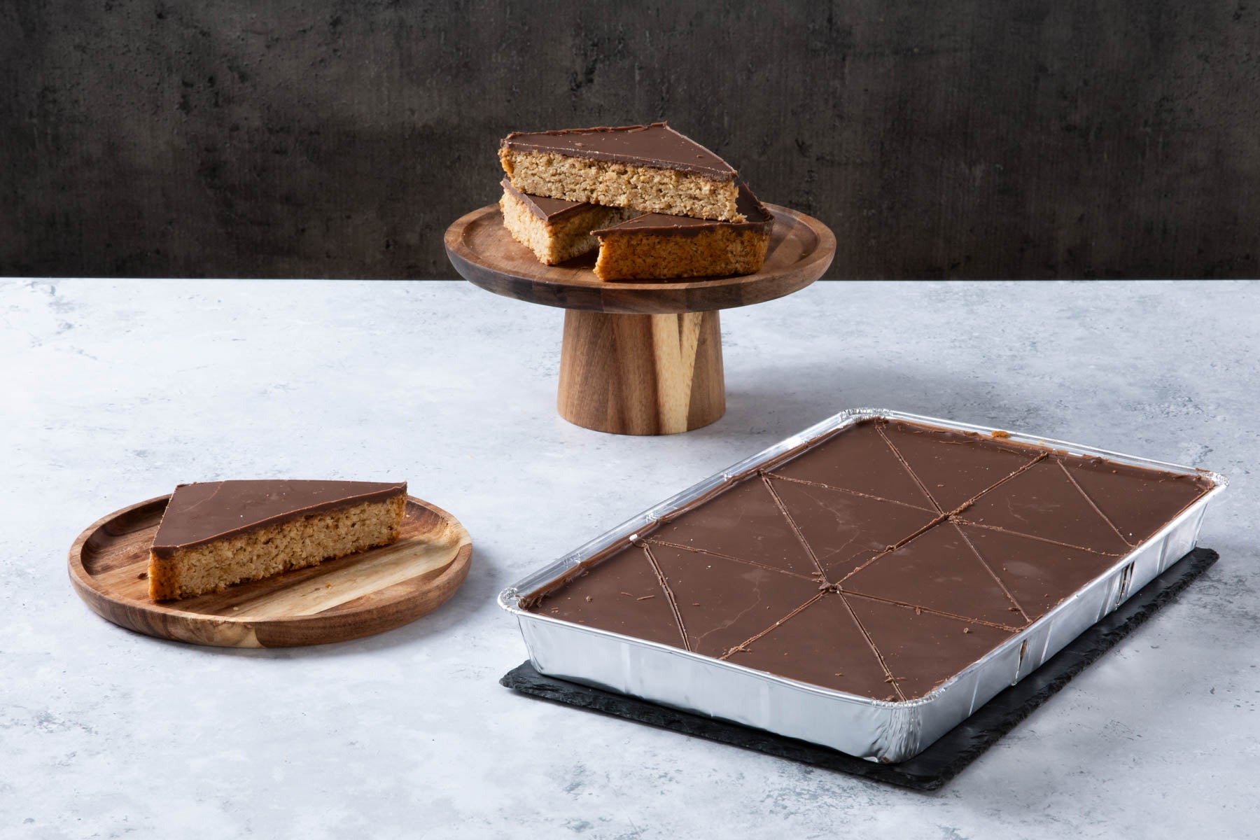 Chocolate-topped oat traybake slices on wooden plates.
