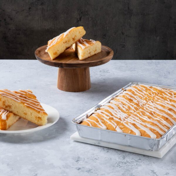Lemon drizzle cake slices with white icing in a baking tray.