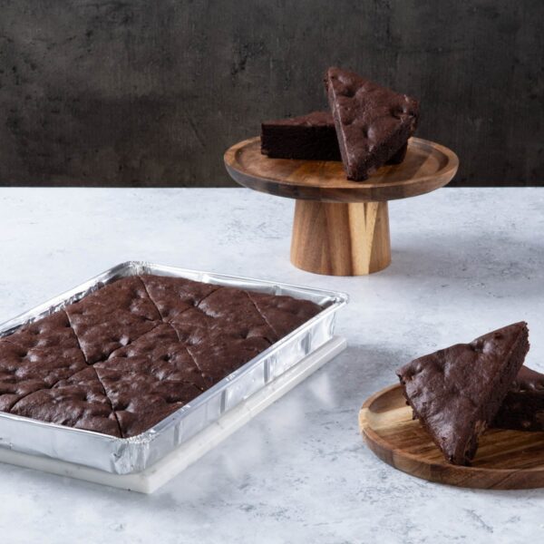 Chocolate cake with creamy frosting and chocolate topping on a wooden board.