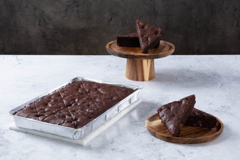 Chocolate cake with creamy frosting and chocolate topping on a wooden board.