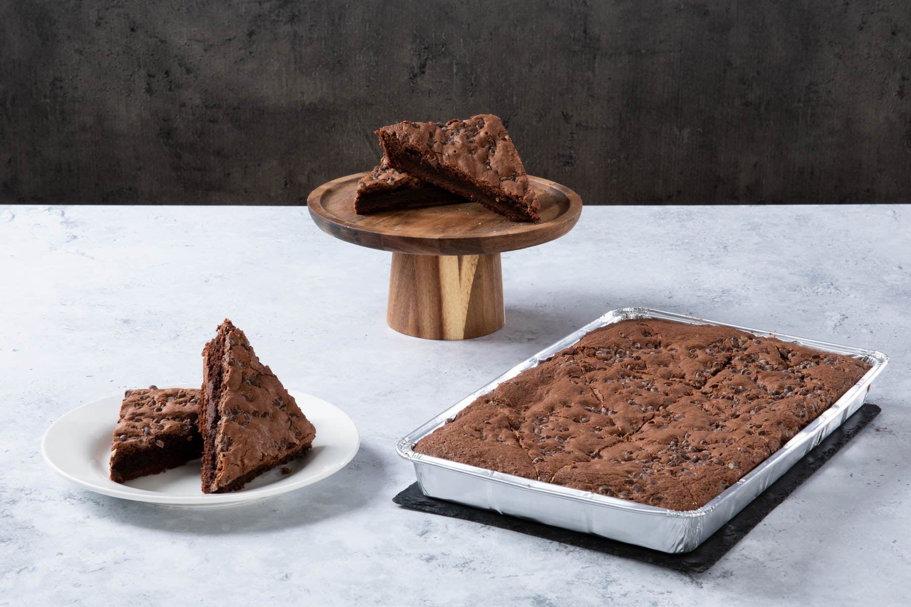 Chocolate cake with creamy frosting and chocolate topping on a wooden board.