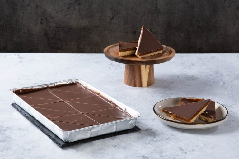 Chocolate caramel shortbread slices with a chocolate topping on a cake stand and plate.