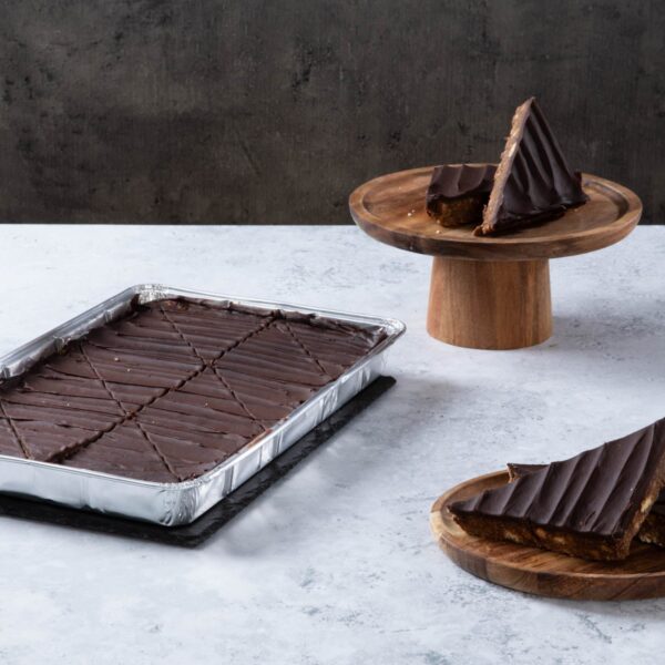 Chocolate cake with creamy frosting and chocolate topping on a wooden board.