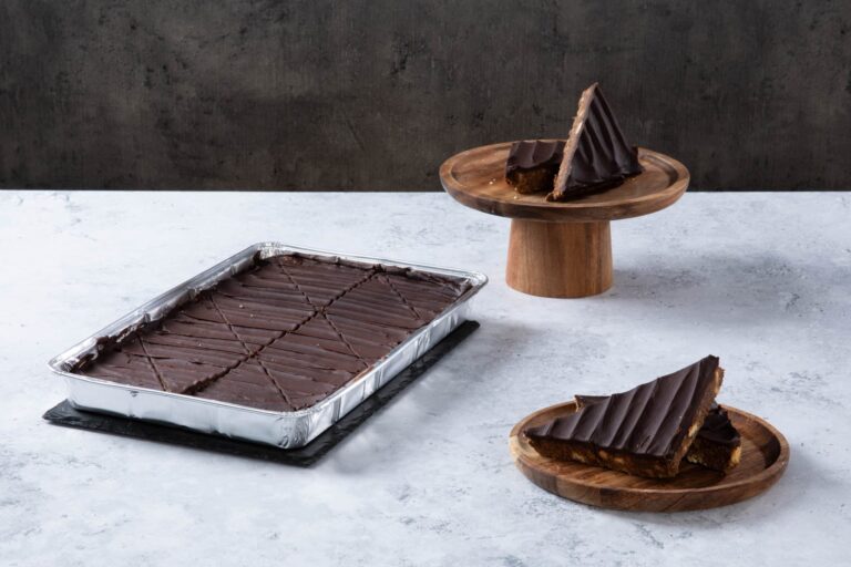 Chocolate cake with creamy frosting and chocolate topping on a wooden board.