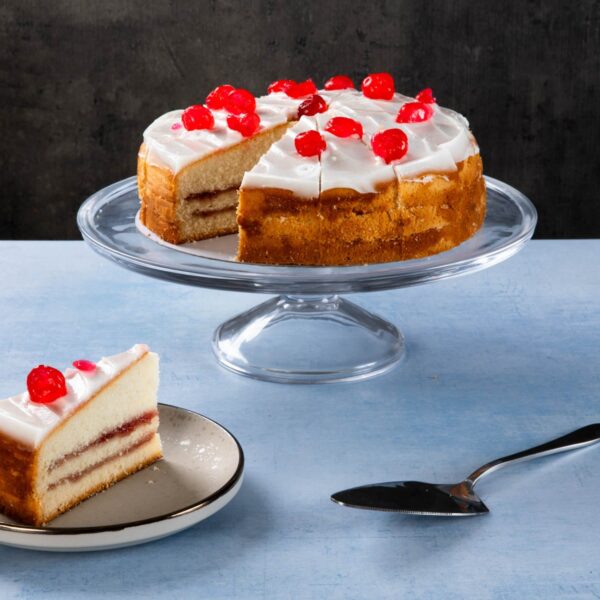 Cherry-topped sponge cake with white frosting on a glass cake stand.
