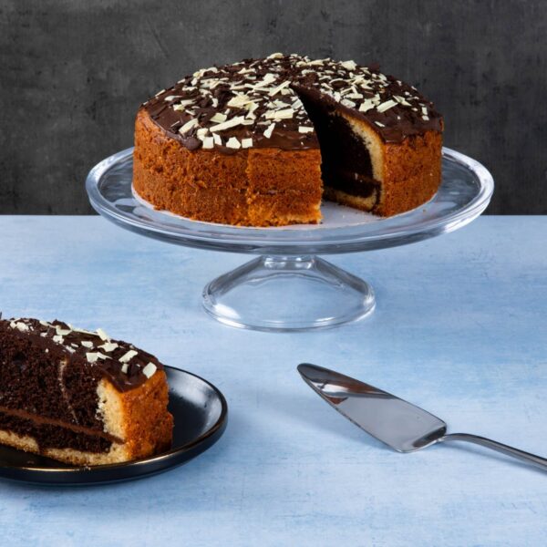 Chocolate cake with chocolate topping and white chocolate shavings on a glass cake stand.