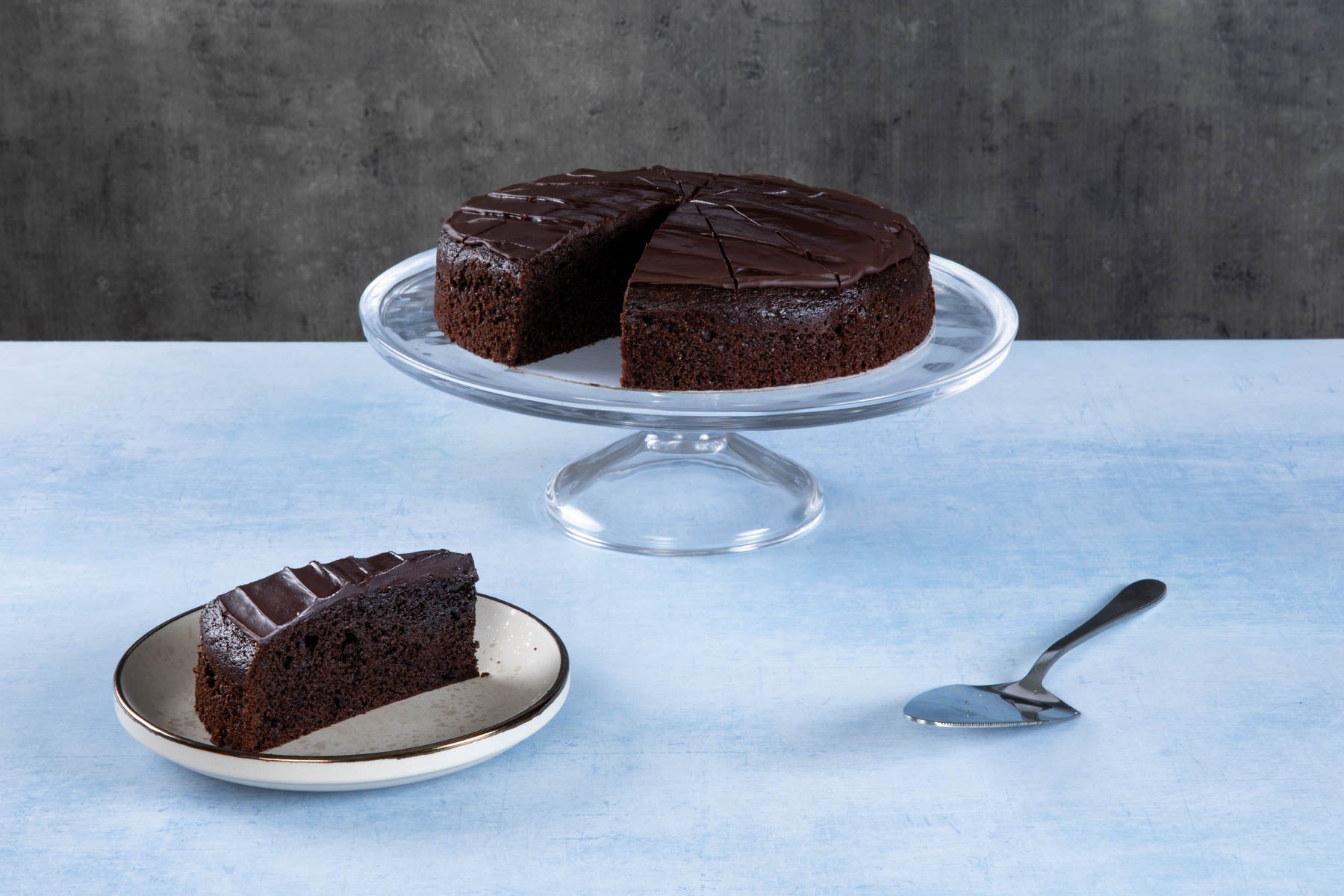 Chocolate cake with creamy frosting and chocolate topping on a wooden board.