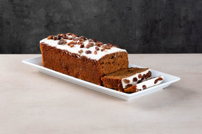 Carrot and raisin loaf cake with white icing and sliced pieces.