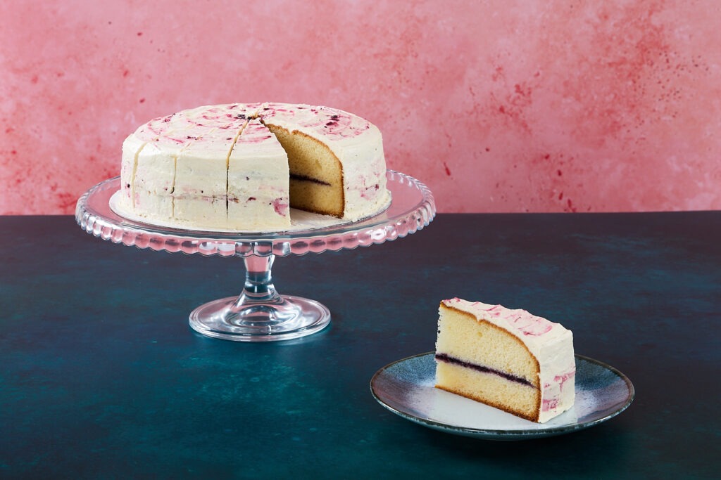 Banana and blueberry cake with pink icing and a sliced piece.