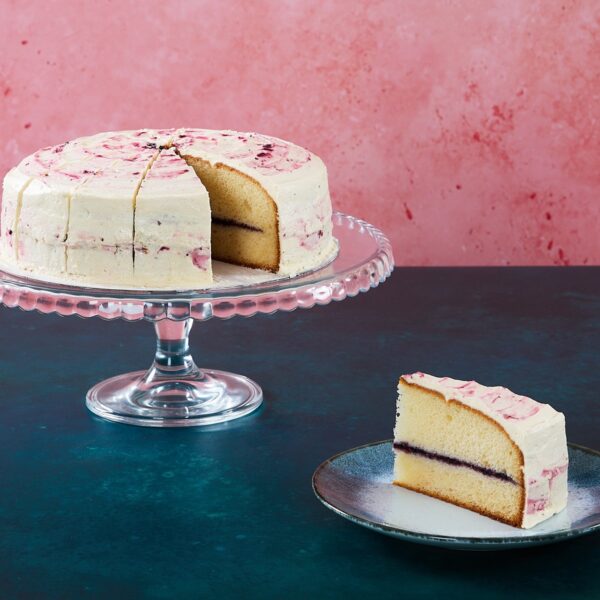 Banana and blueberry cake with pink icing and a sliced piece.