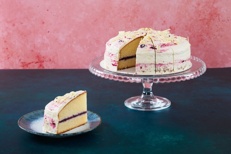 Lemon and blueberry cake with white chocolate topping on a glass cake stand.